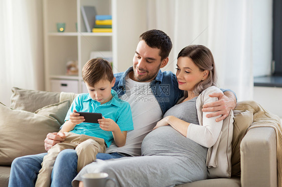 家庭,怀孕技术快乐的怀孕母亲,父亲小儿子坐家里的沙发上智能手机家里智能手机的幸福家庭图片