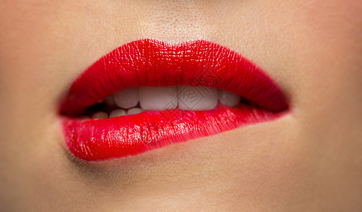 美,化妆嘴的表达用红色口红咬下唇的女人脸用红色口红咬嘴唇的女人特写图片