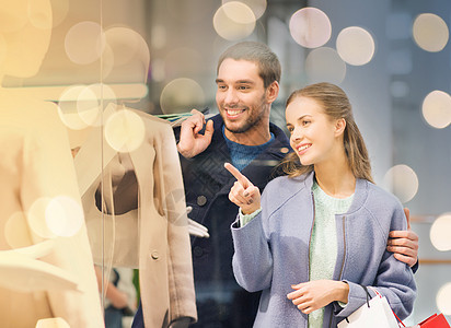 销售,消费主义人们的快乐的轻夫妇,购物袋指着购物中心的橱窗快乐的轻夫妇带着购物袋商场图片