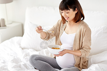 怀孕,人们早餐的快乐的亚洲孕妇家里卧室的床上吃麦片快乐的孕妇家吃麦片图片