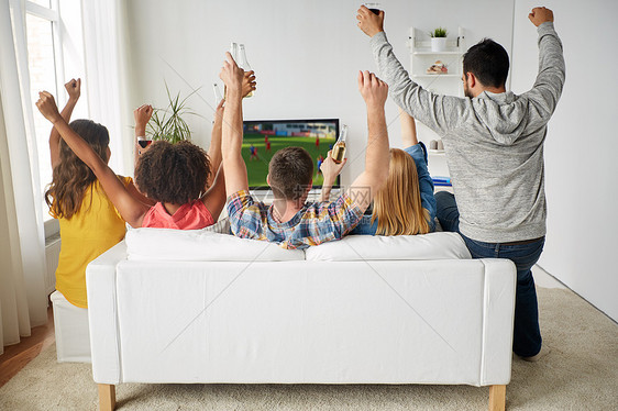 友谊休闲人的快乐的朋友与含酒精的啤酒坐沙发上,家里看足球足球比赛啤酒的朋友家里看电视上的足球图片