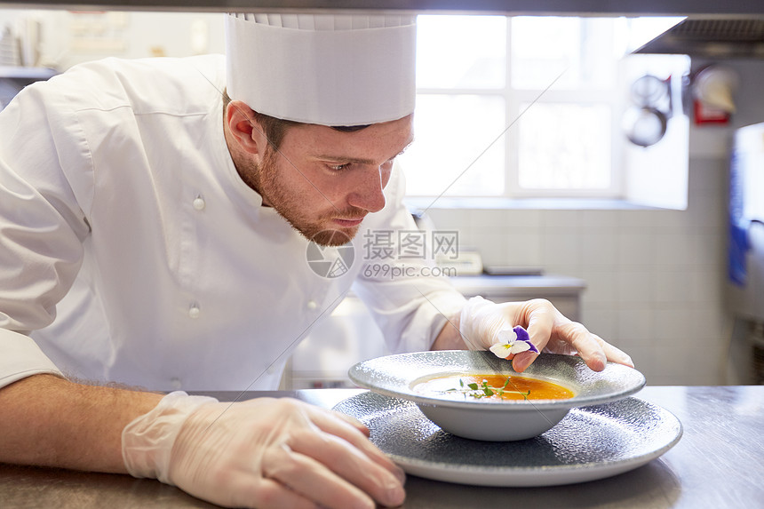 食物烹饪,职业人的快乐的男厨师烹饪服务装饰盘子的汤与花餐厅厨房快乐的男厨师餐厅厨房烹饪食物图片