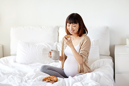 怀孕,休息,人早餐的快乐的怀孕亚洲妇女喝杯茶,床上吃饼干家里的卧室快乐的孕妇家床上吃饼干图片