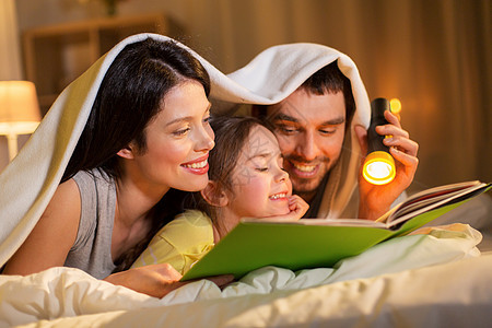 人们家庭的快乐的母亲,父亲小女儿床上阅读书,晚上躺家里的毯子下快乐的家庭阅读书晚上床上家图片