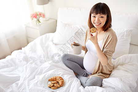 怀孕,休息,人早餐的快乐的怀孕亚洲妇女喝杯茶,床上吃饼干家里的卧室快乐的孕妇家床上吃饼干图片