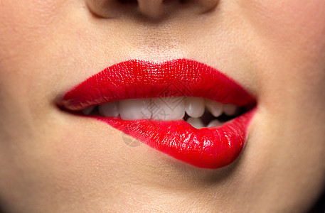 美,化妆嘴的表达用红色口红咬下唇的女人脸用红色口红咬嘴唇的女人特写背景图片