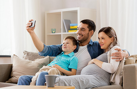 家庭,怀孕技术快乐的怀孕母亲,父亲小儿子自拍与智能手机坐家里的沙发上幸福的家庭家里用智能手机自拍幸福的家庭图片