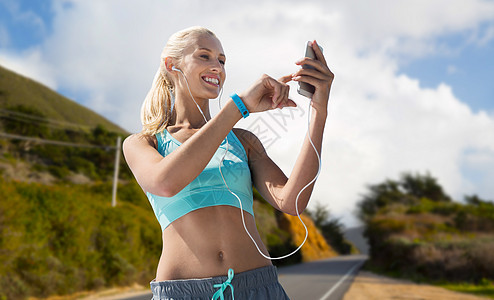 运动,技术健康的生活方式微笑的轻妇女与智能手机,耳机健身跟踪器听音乐大苏尔山道路背景加利福尼亚智能手机图片
