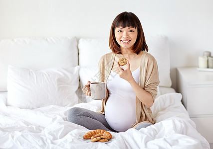 怀孕,休息,人早餐的快乐的怀孕亚洲妇女喝杯茶,床上吃饼干家里的卧室快乐的孕妇家床上吃饼干快乐的孕妇家床上图片