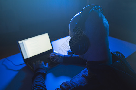 网络犯罪,黑客技术黑客与耳机用笔记本电脑进行网络攻击窃听黑暗的房间黑客黑暗的房间里用耳机笔记本电脑上打背景