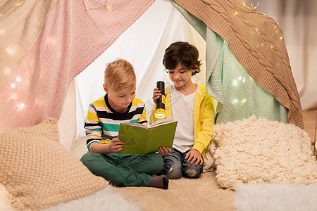 童,友谊潮湿的快乐的小男孩阅读书与火炬灯孩子帐篷帐篷家里快乐的男孩家孩子们的帐篷里看书快乐的男孩家图片
