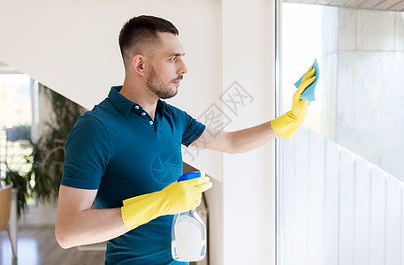 家庭人们的男人戴着橡胶手套,家里用抹布喷雾器清洁窗户戴橡胶手套的人用抹布清洁窗户戴橡胶手套的人用抹布清洁窗户图片