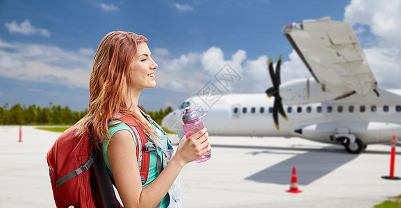 航空旅行,旅游旅行微笑的旅游妇女与背包瓶装水飞机上的机场背景带背包的旅游妇女乘飞机旅行带背包的旅游妇女乘飞机图片