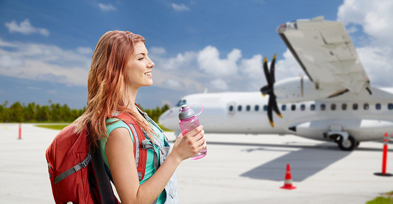 航空旅行,旅游旅行微笑的旅游妇女与背包瓶装水飞机上的机场背景带背包的旅游妇女乘飞机旅行带背包的旅游妇女乘飞机图片