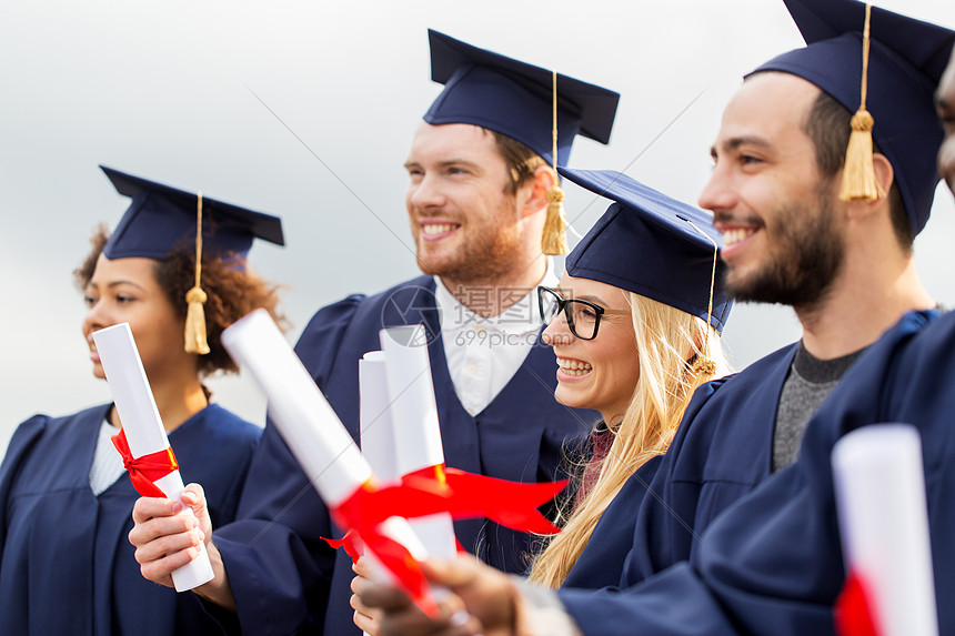 教育毕业人的群快乐的国际学生穿着迫击炮板学士学位礼服与文凭文凭的迫击炮板上快乐的学生文凭的迫击炮板上快