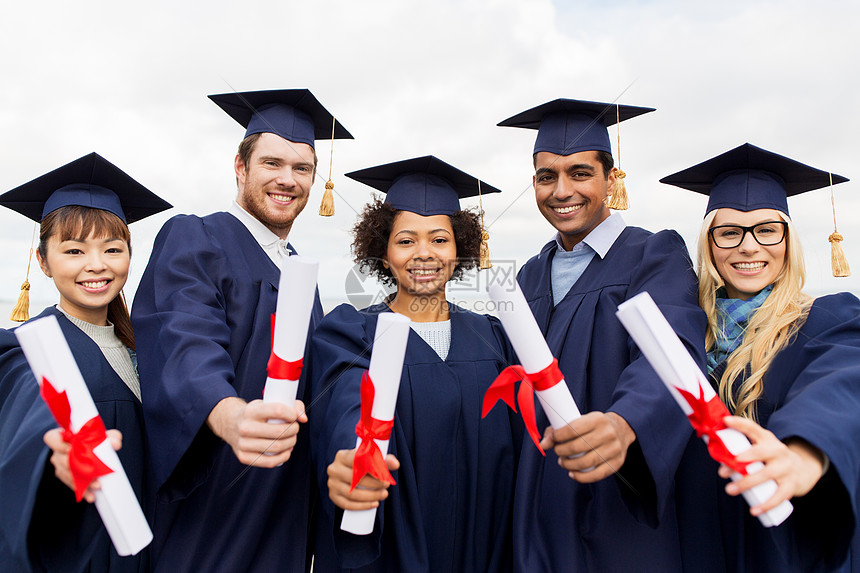 教育毕业人的群快乐的国际学生穿着迫击炮板学士学位礼服与文凭文凭的迫击炮板上快乐的学生文凭的迫击炮板上快图片