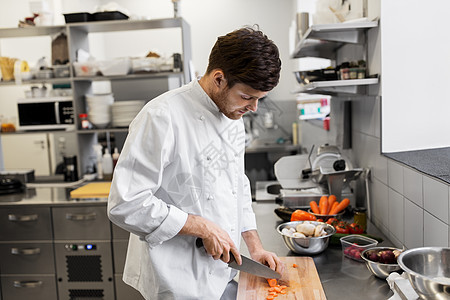 烹饪食物,职业人的快乐的男厨师用刀切胡萝卜餐厅厨房的砧板上饭快乐的男厨师餐厅厨房烹饪食物快乐的男厨师图片