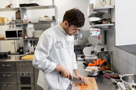 烹饪食物,职业人的快乐的男厨师用刀切胡萝卜餐厅厨房的砧板上饭快乐的男厨师餐厅厨房烹饪食物快乐的男厨师图片