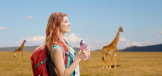 冒险,旅行,旅游,徒步旅行人们的微笑的轻女人带着背包瓶水长颈鹿非洲草原的背景快乐的女人带着背包非洲草原上图片