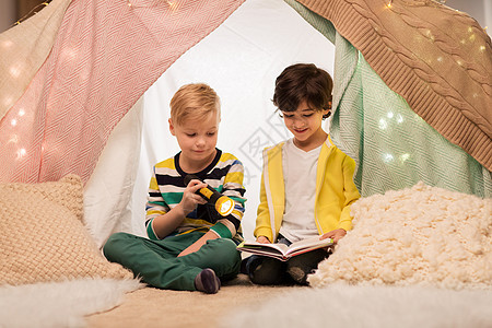 童,友谊潮湿的快乐的小男孩阅读书与火炬灯孩子帐篷帐篷家里快乐的男孩家孩子们的帐篷里看书快乐的男孩家图片