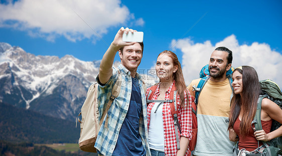 技术,旅游,徒步旅行人们的群微笑的朋友背包阿尔卑斯山背景上用智能手机自拍背包的朋友用智能手机自拍图片