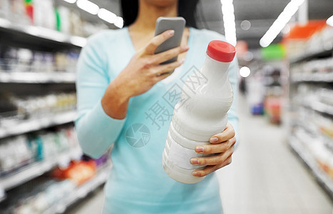 销售,购物,消费主义人的轻的妇女与智能手机持奶瓶杂货店超市智能手机的女人超市买牛奶智能手机的女人图片