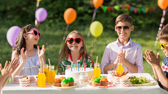假期,童庆祝快乐的孩子蛋糕上着蜡烛,坐夏天的花园聚会上,为生日女孩鼓掌快乐的孩子夏天的生日聚会上吃蛋糕图片