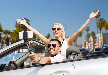 车智汇公路旅行,技术旅行快乐的夫妇驾驶敞篷汽车,并智能手机拍摄自拍棒威尼斯海滩背景加利福尼亚幸福的夫妇汽车上用智背景