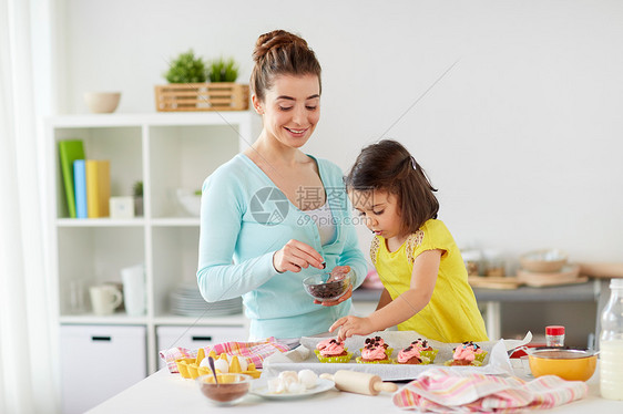 家庭,烹饪人们的快乐的母亲小女儿家庭厨房用巧克力洒来制作装饰纸杯蛋糕快乐的母亲女儿家纸杯蛋糕图片