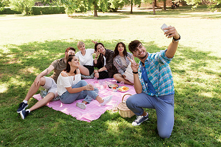 友谊休闲技术群快乐的微笑朋友夏季公园的野餐毯上用智能手机自拍朋友们野餐时用智能手机自拍图片
