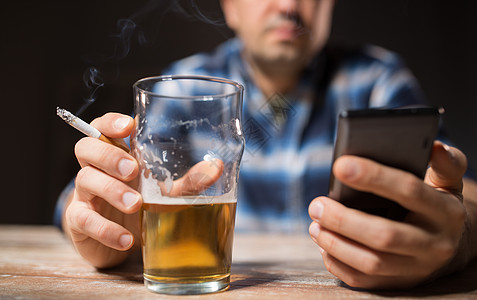 吸烟伤肺酒精男酒精与智能手机喝啤酒吸烟晚上手机的男人喝酒抽烟背景