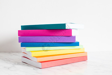 五颜六色的书彩虹的颜色中被勾勒出来把书堆放白色墙壁附近的架子上五颜六色的书籍收藏图片