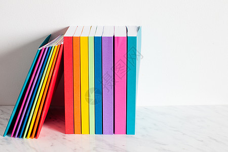 五颜六色的书彩虹的颜色中被勾勒出来把书堆放白色墙壁附近的架子上五颜六色的书籍收藏图片