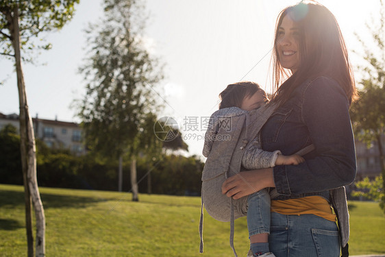 妈妈抱着蹒跚学步的孩子轻的母亲公园里抱着小蹒跚学步的孩子图片
