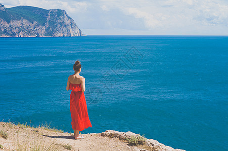 户外生活方式照片的女人穿着红色的衣服看着大海旅行背景旅游业图片