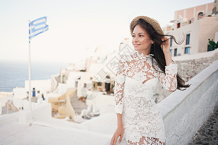穿着白色连衣裙草帽的快乐女人桑托里尼岛享受假期OIA看爱琴海欧洲夏季旅游目的地希腊岛屿背景图片