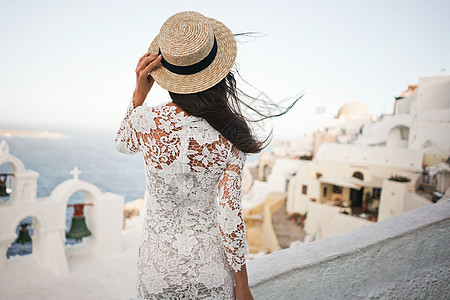 穿着白色连衣裙草帽的快乐女人桑托里尼岛享受假期OIA看爱琴海欧洲夏季旅游目的地希腊岛屿背景图片