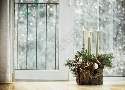 冬季舒适的家居装饰节日气氛与燃烧的蜡烛,冷杉枝雪花客厅的窗户与降雪装饰的降临花圈背景图片