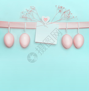 复活节贺卡上挂着淡蓝色绿松石背景丝带上的淡粉色鸡蛋创造的问候布局与为您的文本图片
