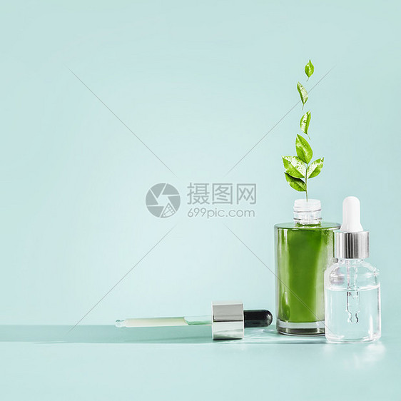 草药部护肤化妆品瓶与滴管吸管蓝色背景天然血清油制品与绿色药用草药叶子,正视图品牌模型图片