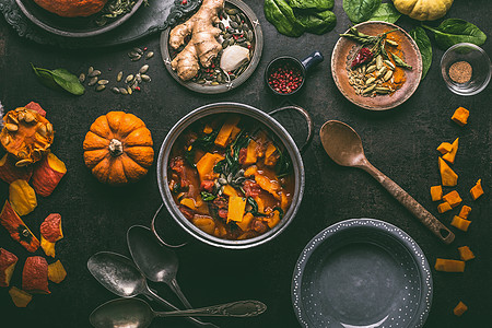 南瓜炖菠菜生姜烹饪锅与勺子碗黑暗的厨房桌子背景,顶部视图,平躺素食秋季季节食物背景图片