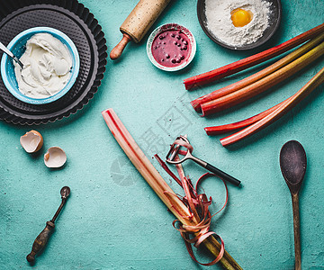 大黄脱皮新鲜的红色大黄梗与剥皮机厨房桌子背景与烹饪烘焙工具,顶部视图季节食物图片