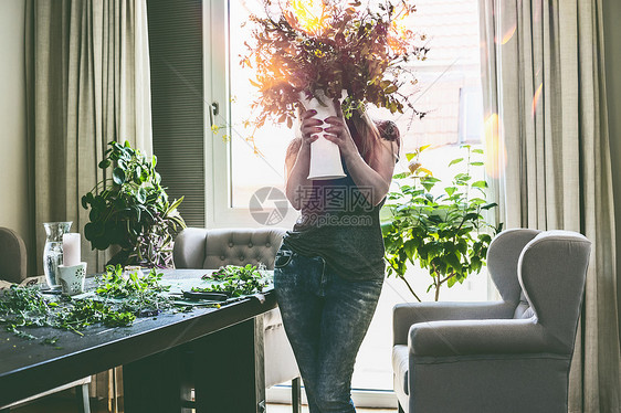 漂亮的女人着花瓶,手里着夏天的野花,客厅里,窗户上桌子耳朵扶手椅家庭生活方式装饰理念图片