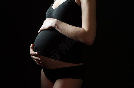 黑色背景上穿黑色衣服的孕妇的中段图片