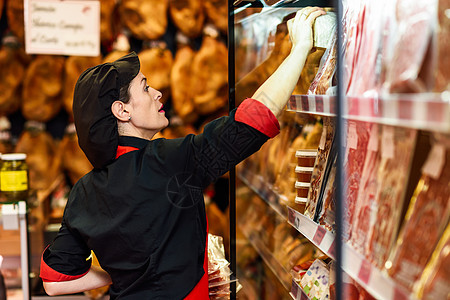 女工人肉店产品的肖像香肠包装火腿奶酪的冷藏展示箱图片