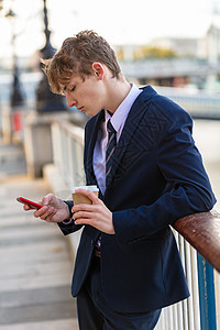 男轻成青少穿着西装领带,用智能手机进行社交媒体喝外卖咖啡图片