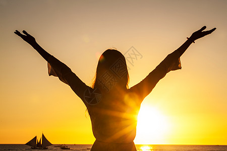 自由快乐的女人举手臂,日落的背景下看着太阳大海自由快乐的女人举手臂背景图片
