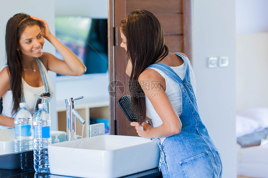 微笑的轻女人看着镜子,家里的浴室里用梳子梳头女人刷头发图片