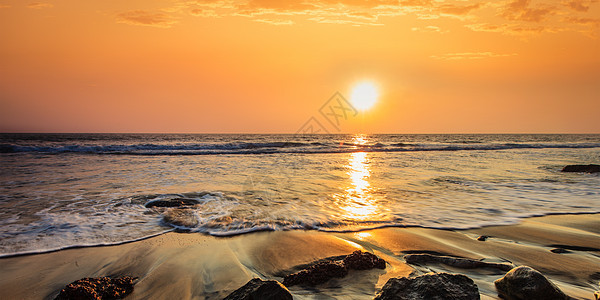 热带海滩度假背景日落时海滩上波浪岩石的全景与美丽的云景日落海滩上的波浪岩石图片