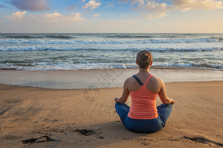 女人瑜伽冥想放松帕德马萨纳莲花阿萨纳姿势与中国泥德拉户外热带海滩日落海滩上瑜伽的女人帕德马萨纳莲花姿势图片